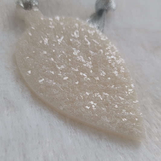 Drop shaped epoxy resin ornament that has a crystalline texture, made with white pigment and a sparkling silver ribbon attached.