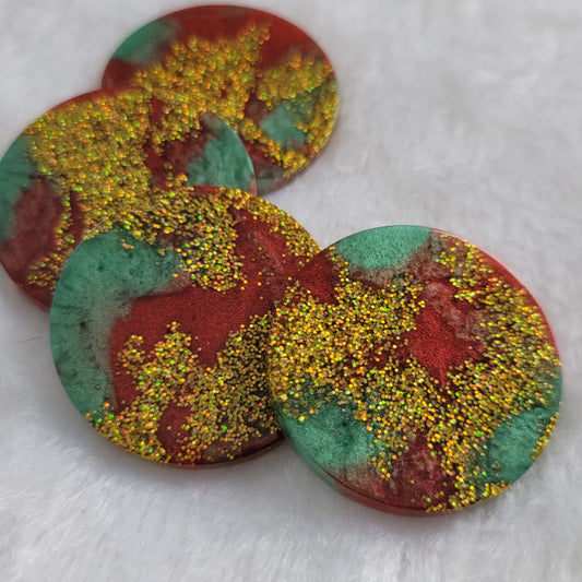 Four round epoxy resin pieces with swirled red and green pigment and gold holographic glitter.