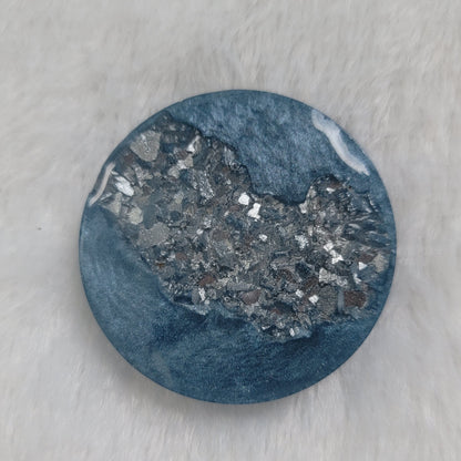 Round epoxy resin piece made with ice blue mica pigment and silver crystalline texture inset running through the center of the piece.