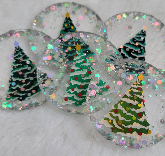 Five round epoxy resin pieces with silver holographic glitter and vinyl Christmas tree designs on them.