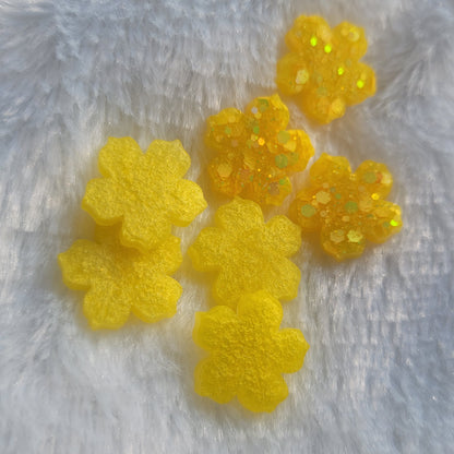 Seven extra small flower blossom shaped epoxy resin pieces, four with shimmering yellow pigment and three with bright yellow glitter.