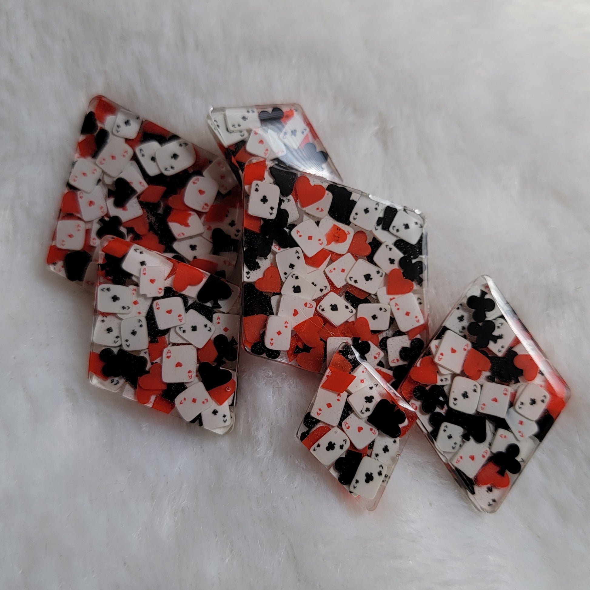 Six diamond shaped epoxy resin pieces, two each in three different sizes, filled with tiny polymer clay pieces shaped like card suits and aces.