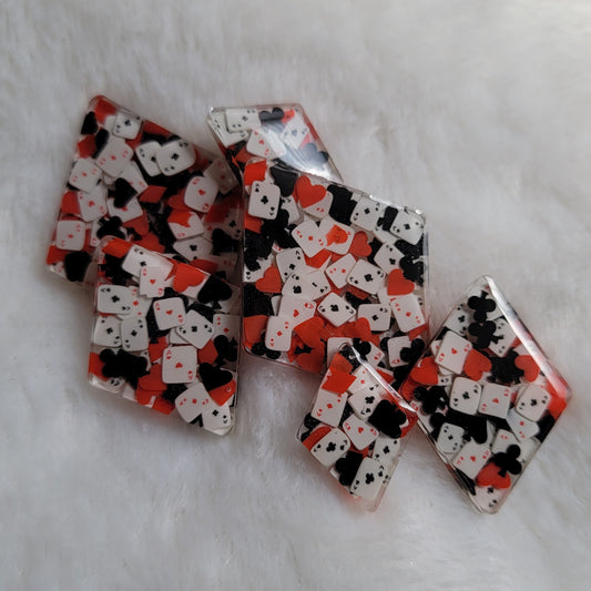 Six diamond shaped epoxy resin pieces, two each in three different sizes, filled with tiny polymer clay pieces shaped like card suits and aces.