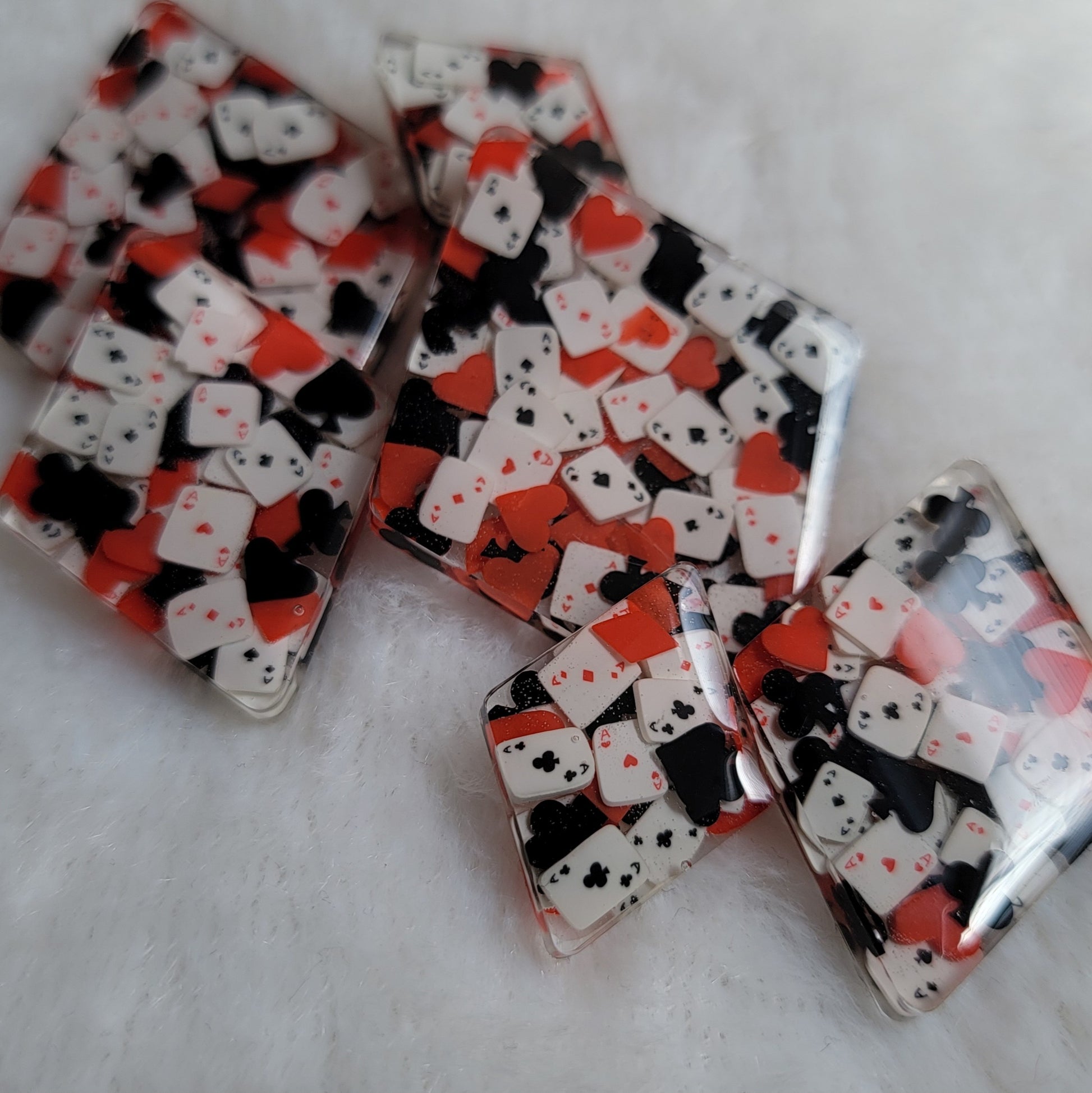 Six diamond shaped epoxy resin pieces, two each in three different sizes, filled with tiny polymer clay pieces shaped like card suits and aces.