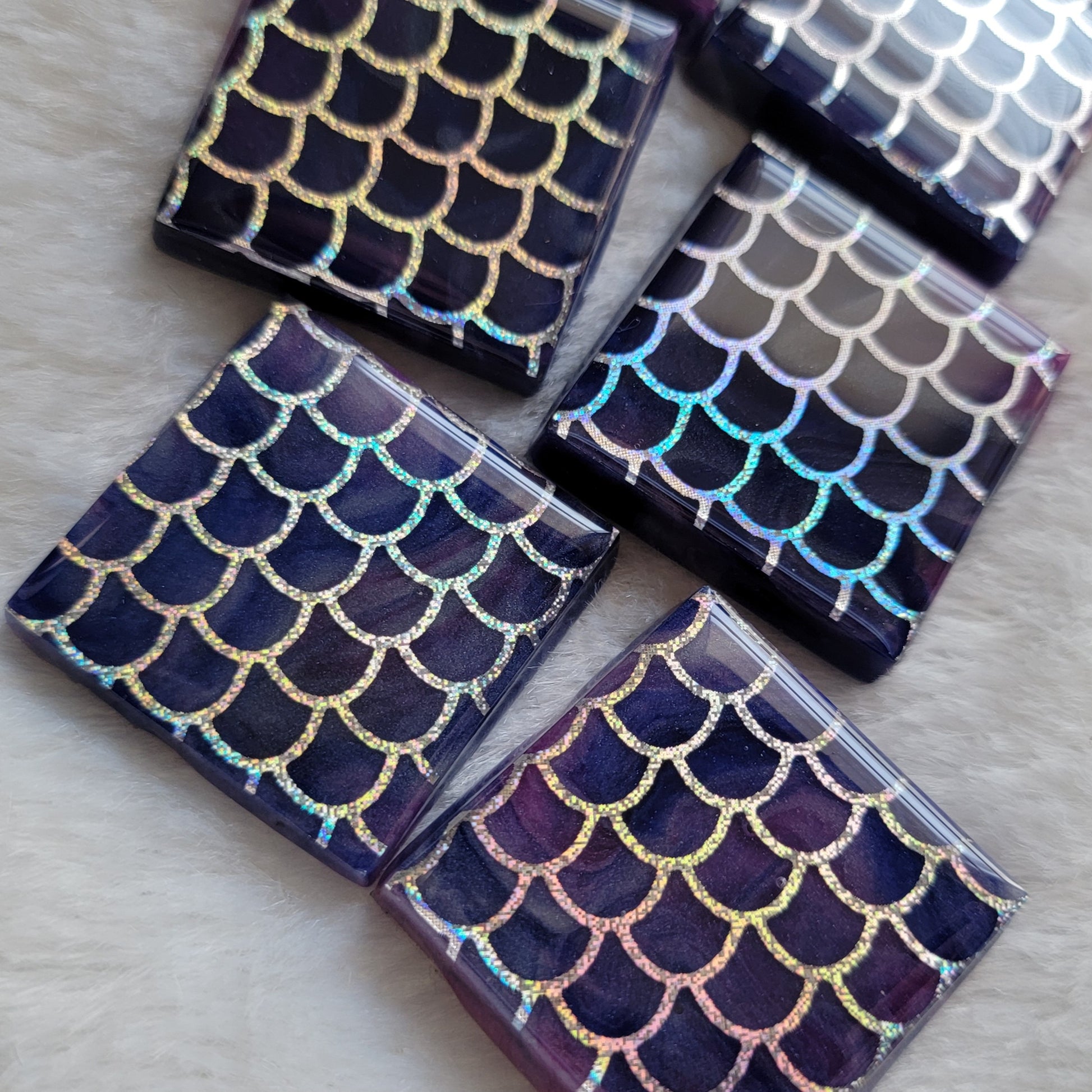 Close up of square epoxy resin pieces, blue and purple swirled bases with holographic silver fish scale design in vinyl.