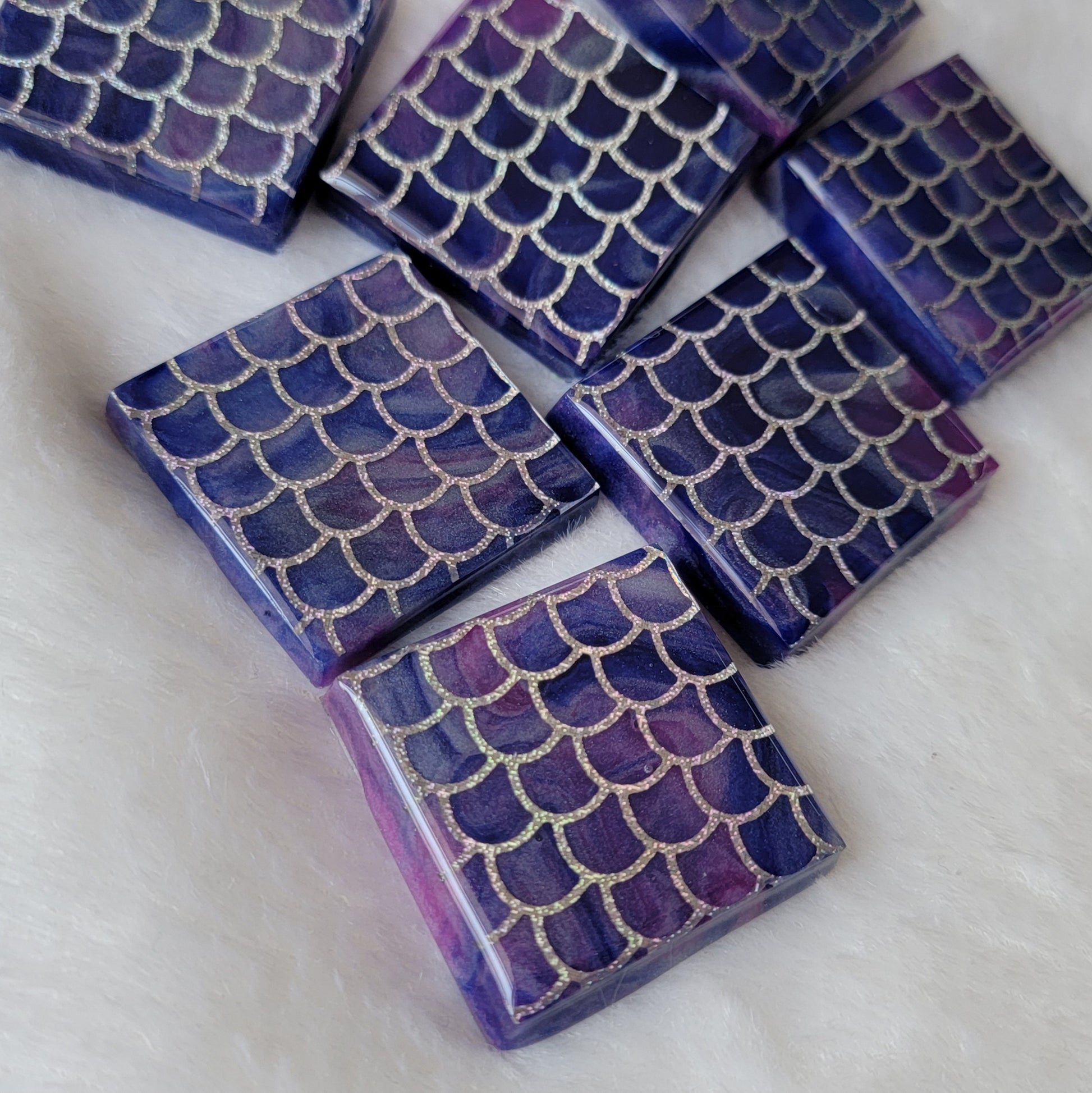 Seven square epoxy resin pieces, blue and purple swirled bases with holographic silver fish scale design in vinyl.