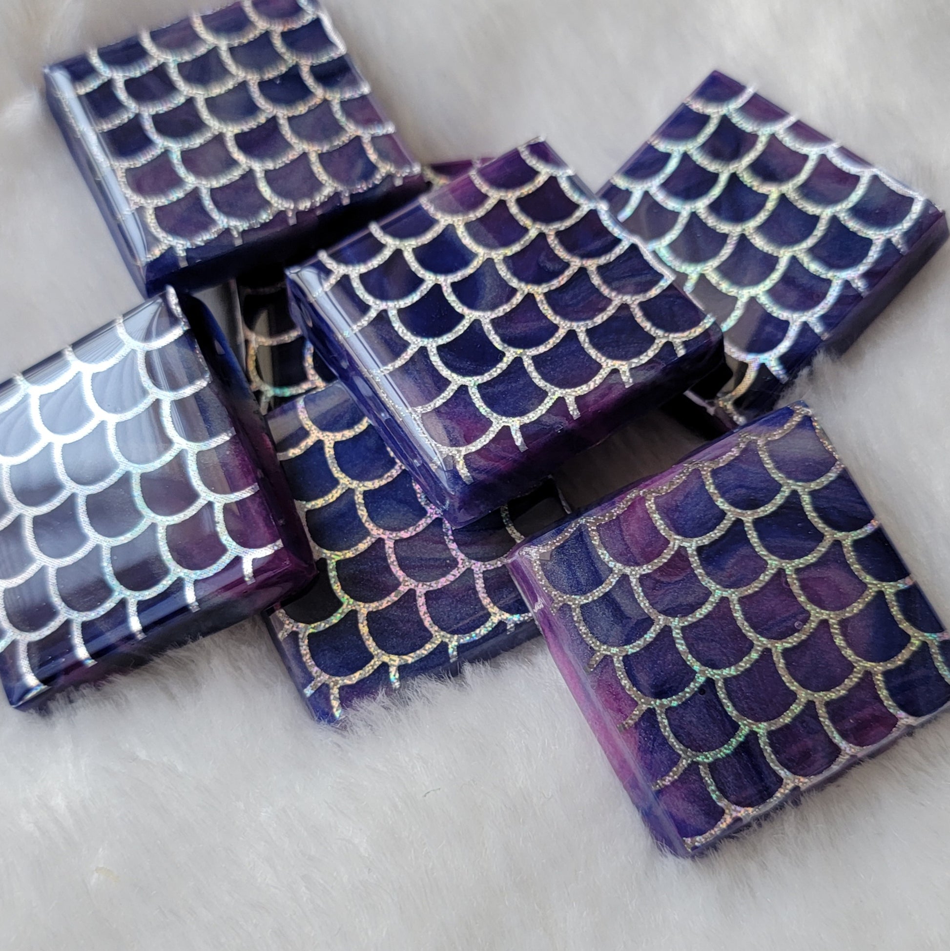 Seven square epoxy resin pieces, blue and purple swirled bases with holographic silver fish scale design in vinyl.