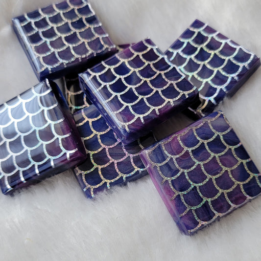 Seven square epoxy resin pieces, blue and purple swirled bases with holographic silver fish scale design in vinyl.