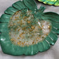 Monstera leaf shaped decorative dish made from epoxy resin, translucent center with gold foil flakes and deep hunter green edges.