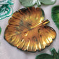 Monstera leaf shaped decorative dish made from epoxy resin, iridescent gold coating over dark green.