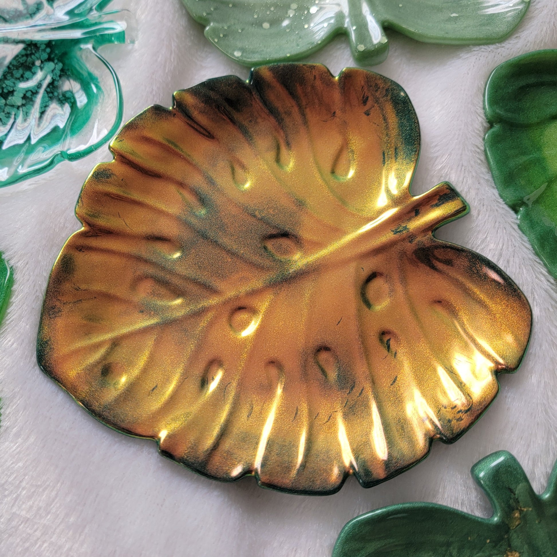Monstera leaf shaped decorative dish made from epoxy resin, iridescent gold coating over dark green.