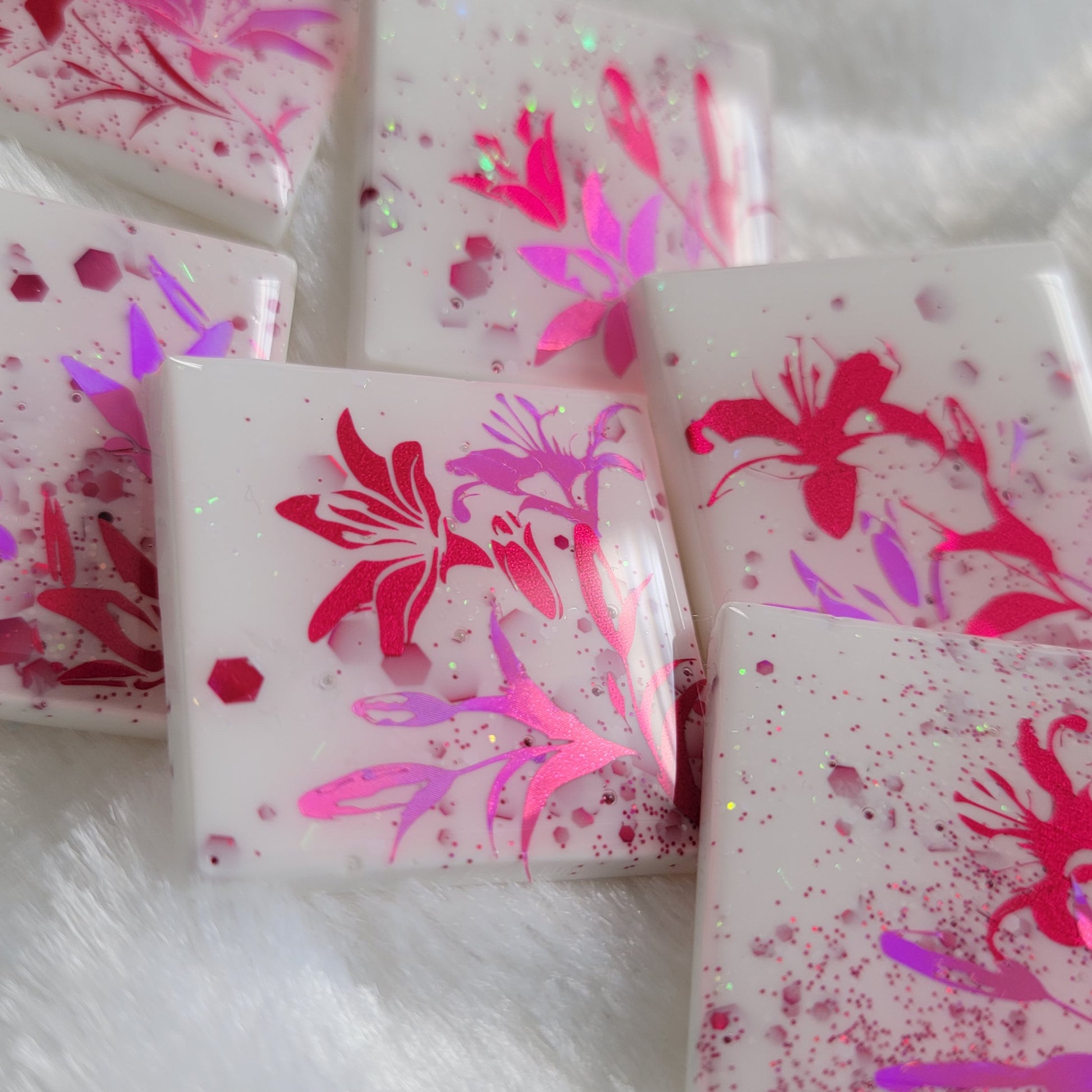 Six square epoxy resin pieces, bases are white with pink and opal glitter and each piece features a unique lily scene in metallic and holographic pink vinyl.