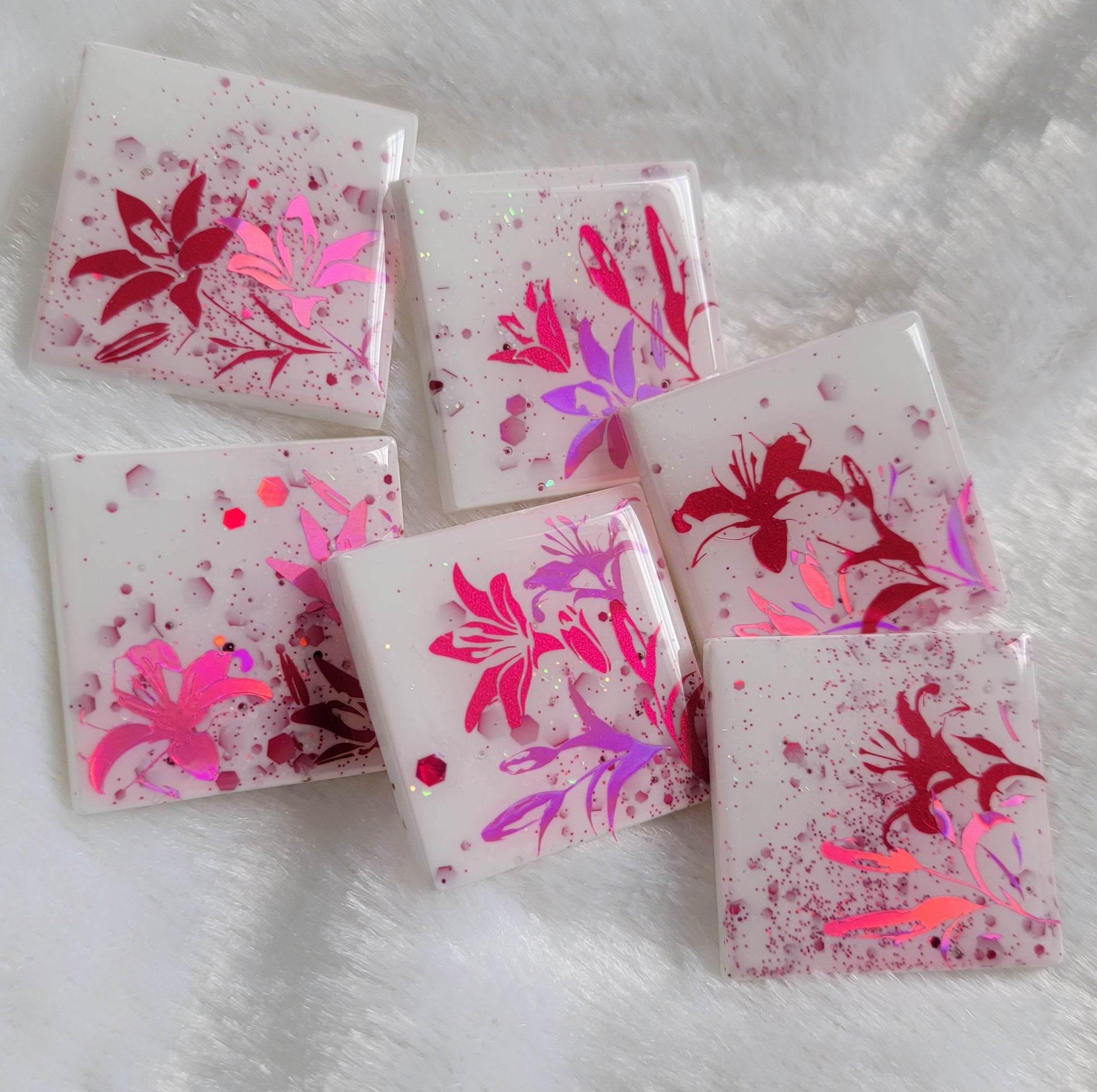Six square epoxy resin pieces, bases are white with pink and opal glitter and each piece features a unique lily scene in metallic and holographic pink vinyl.