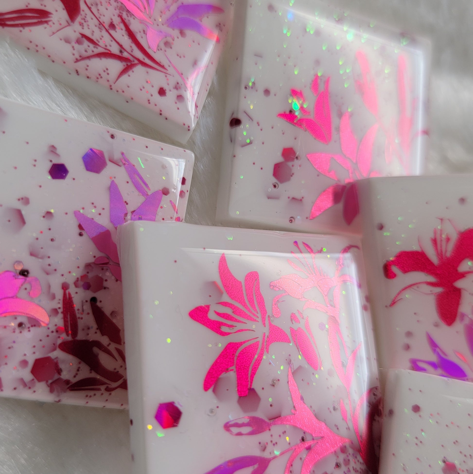 Six square epoxy resin pieces, bases are white with pink and opal glitter and each piece features a unique lily scene in metallic and holographic pink vinyl.