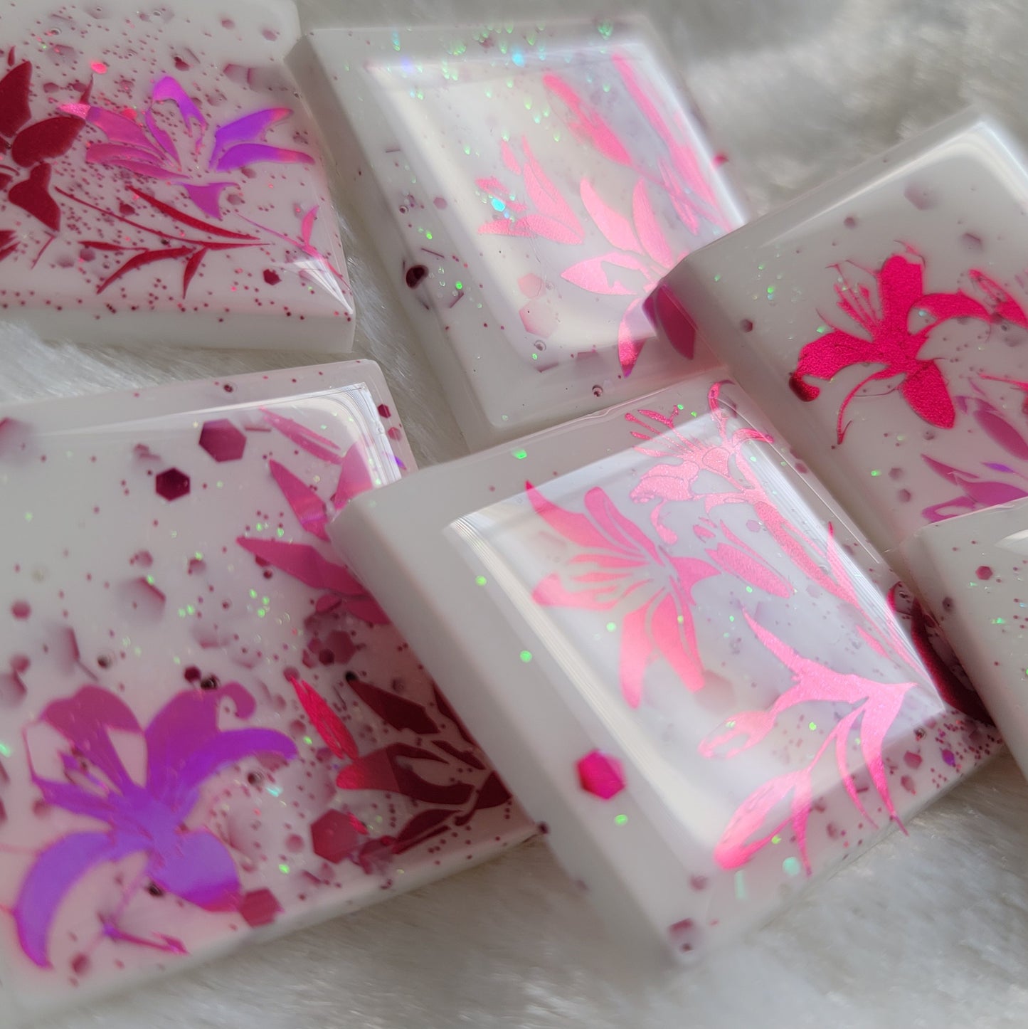 Six square epoxy resin pieces, bases are white with pink and opal glitter and each piece features a unique lily scene in metallic and holographic pink vinyl.
