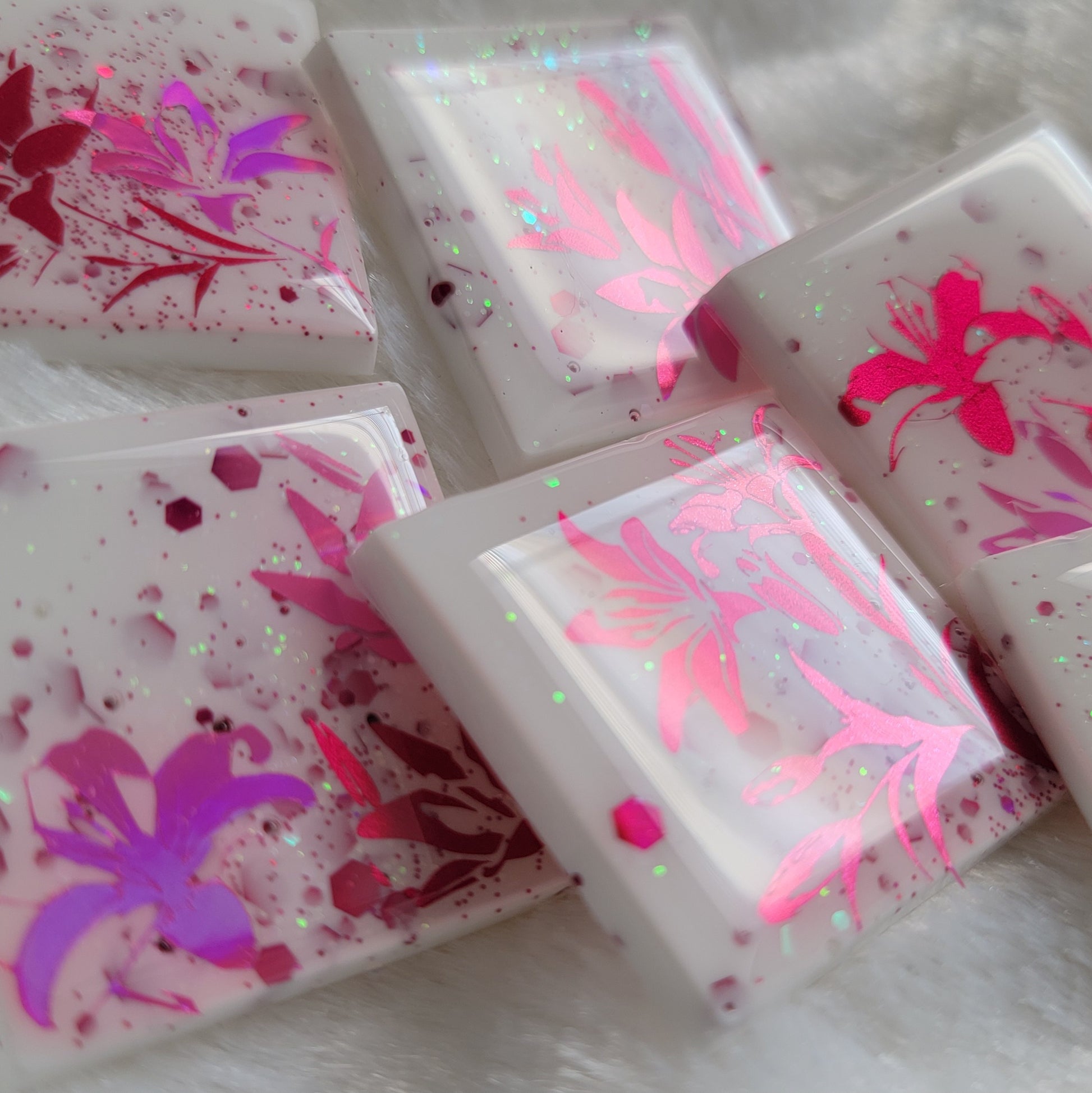 Six square epoxy resin pieces, bases are white with pink and opal glitter and each piece features a unique lily scene in metallic and holographic pink vinyl.