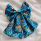 A handmade pet bow with a bold cotton print in ultramarine blue with amber outlines of seashells and starfish, sailor bow style with long showy tails.