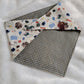 A reversible pet bandana with one side featuring an assortment of camping-themed patterns including a tent, campfire, and backpack, and the other side in a blue gingham plaid. 