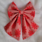 A handmade pet bow made with bright red daisy patterned mesh fabric layered over soft red pinstripe cotton, sailor bow style with long showy tails.