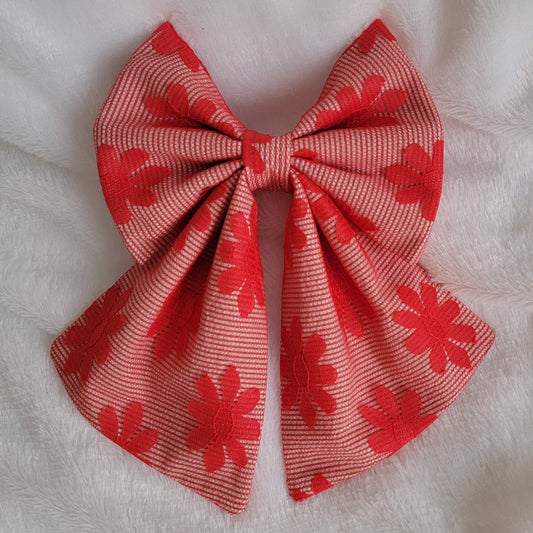 A handmade pet bow made with bright red daisy patterned mesh fabric layered over soft red pinstripe cotton, sailor bow style with long showy tails.