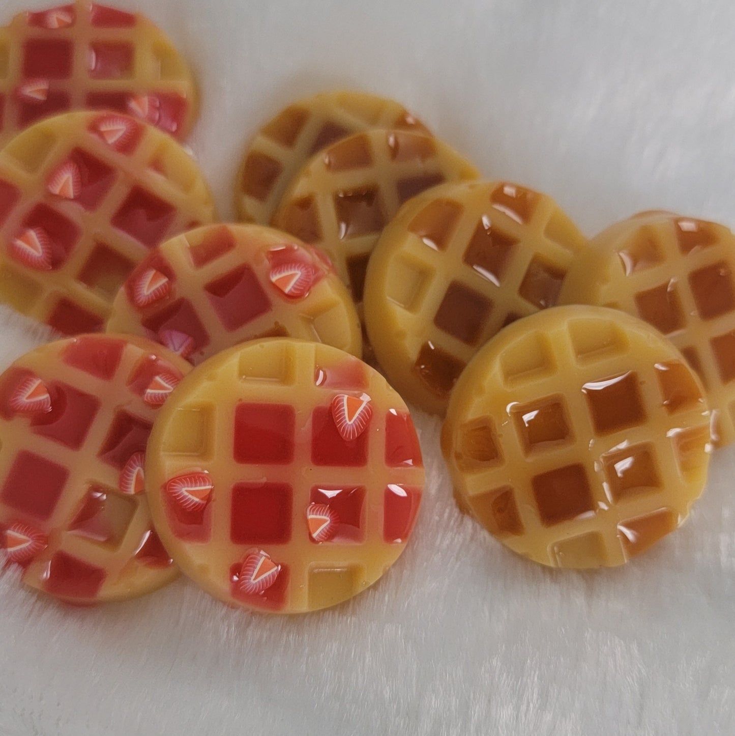 Ten waffle shaped resin pieces, decorated to look like 5 waffles covered with maple syrup and 5 topped with strawberries and jam.