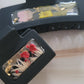 An array of 4-inch and 2-inch black claw clips with open spaces that are filled with pressed flowers and foliage and gold flakes cast in resin.