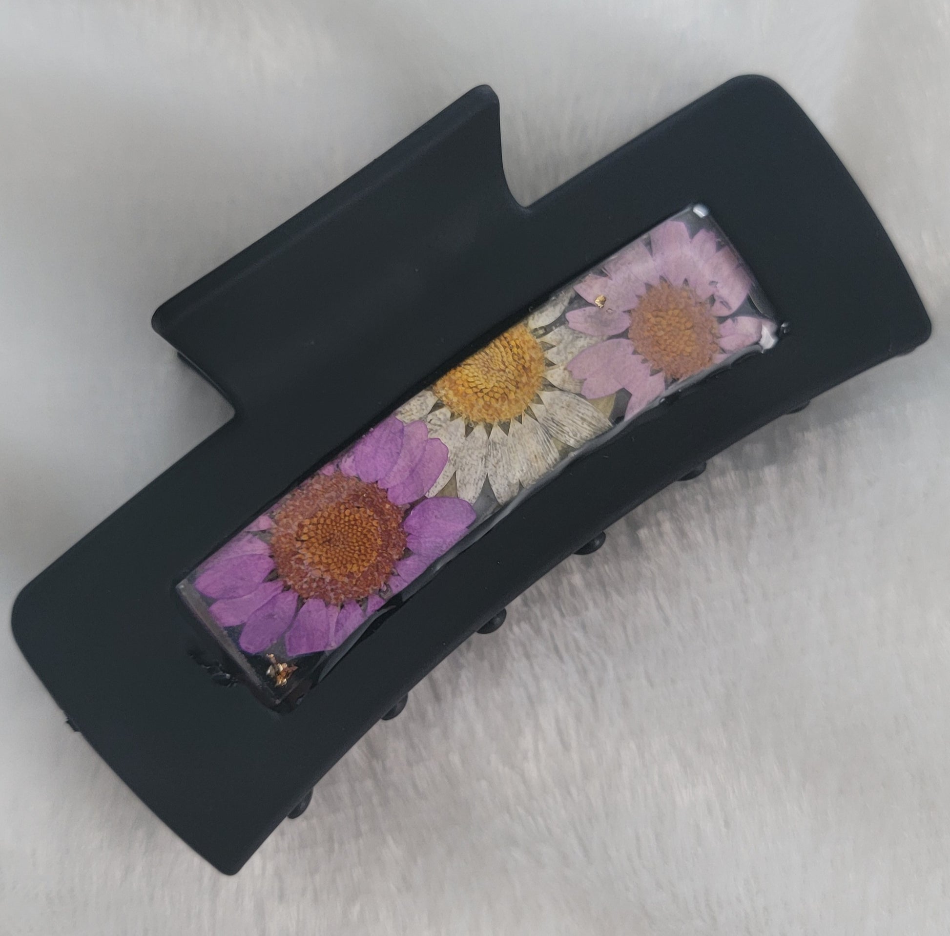 A black 4-inch claw clip with lavender and white pressed flowers cast in resin within an open space in the hair clip.