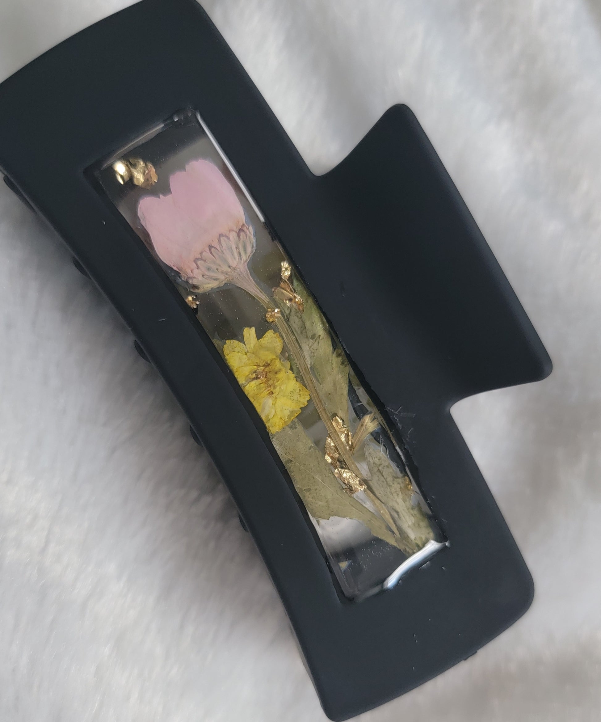 A black 4-inch claw clip with a long stem pink flower and small yellow blossom cast in resin within an open space in the hair clip.