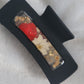A black 4-inch claw clip with red and white pressed flowers cast in resin within an open space in the hair clip.