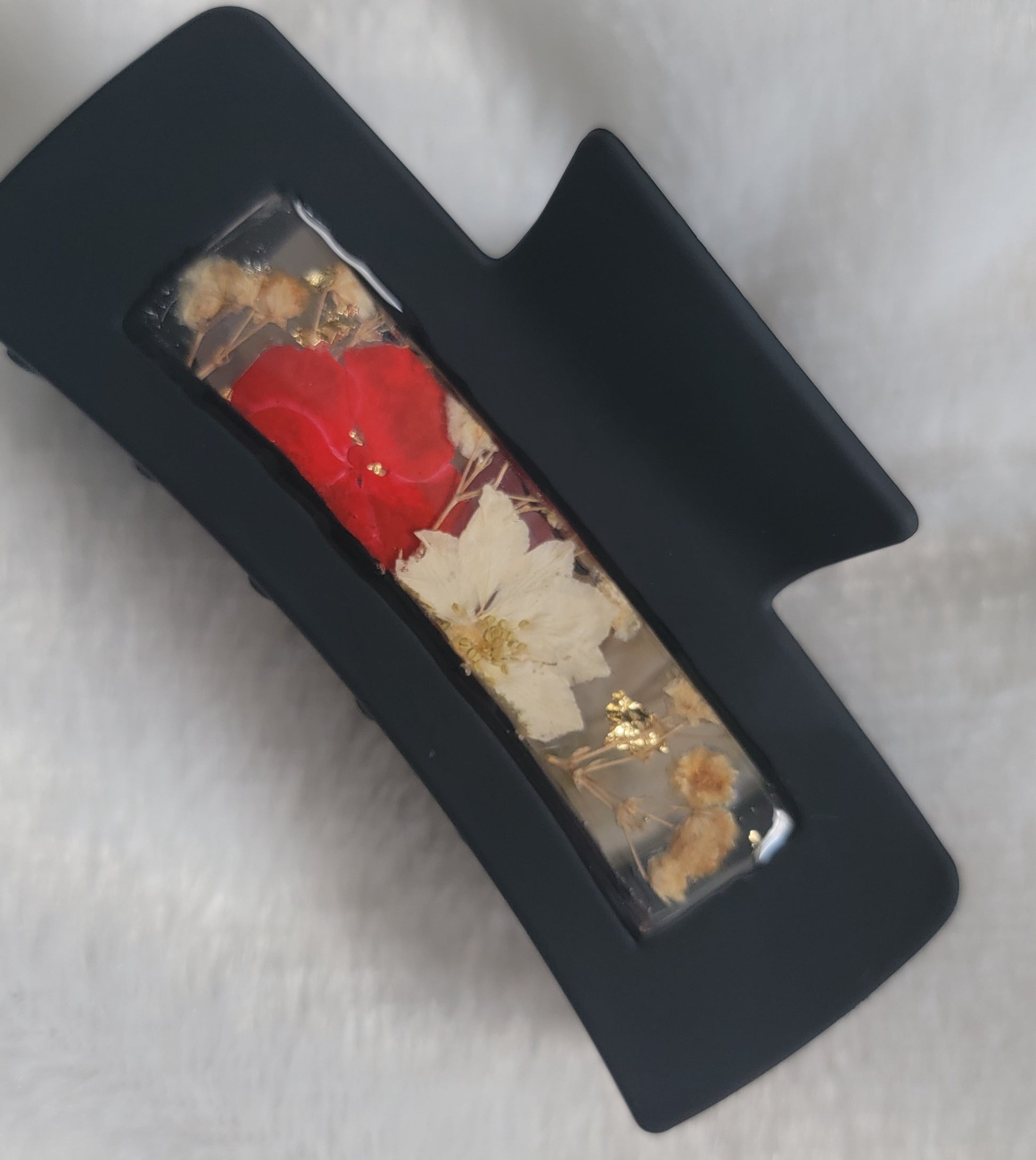 A black 4-inch claw clip with red and white pressed flowers cast in resin within an open space in the hair clip.