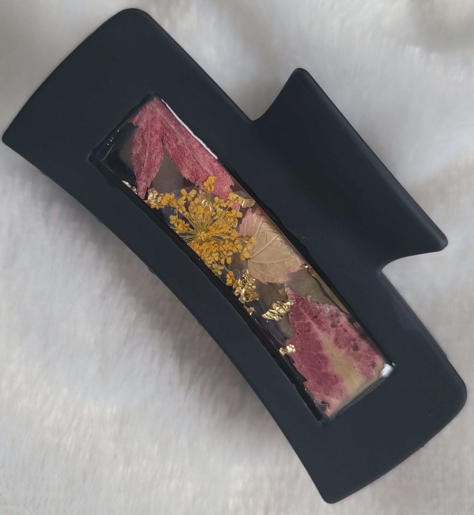 A black 4-inch claw clip with orange pressed flower and fall leaves cast in resin within an open space in the hair clip.