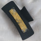 A black 4-inch claw clip with yellow pressed flowers cast in resin within an open space in the hair clip.