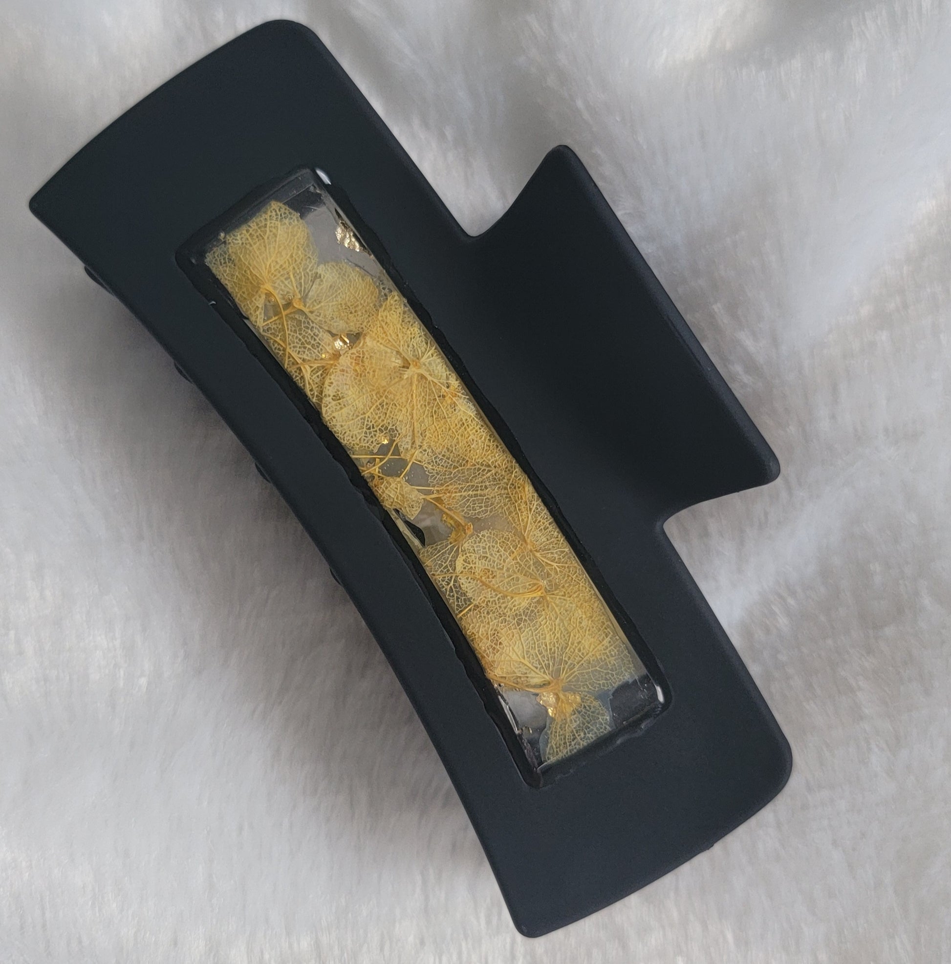 A black 4-inch claw clip with yellow pressed flowers cast in resin within an open space in the hair clip.