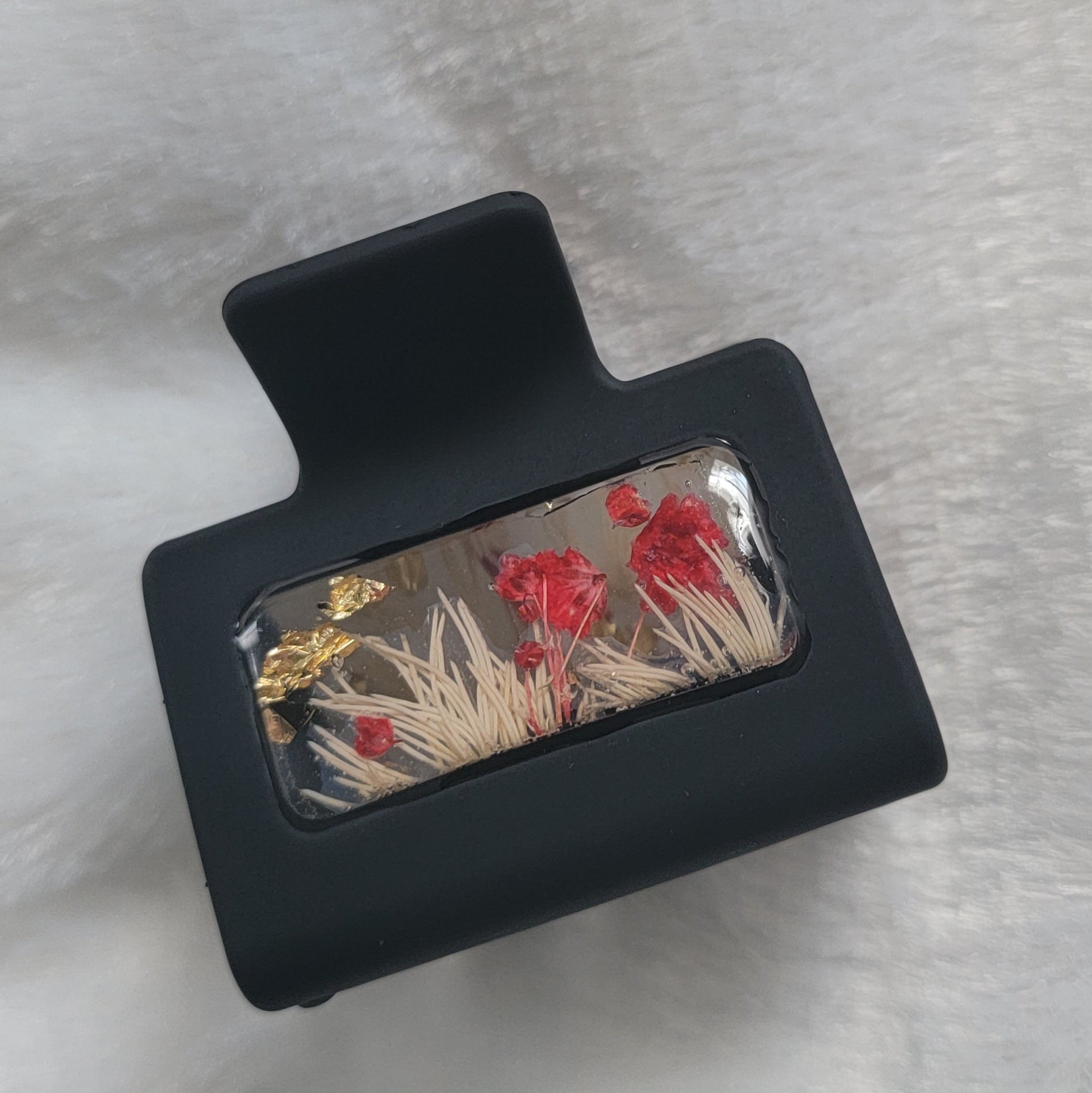 A black 2-inch claw clip with red and white flowers cast in resin within an open space in the hair clip.