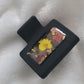 A black 2-inch claw clip with yellow pressed flowers and fall leaves cast in resin within an open space in the hair clip.