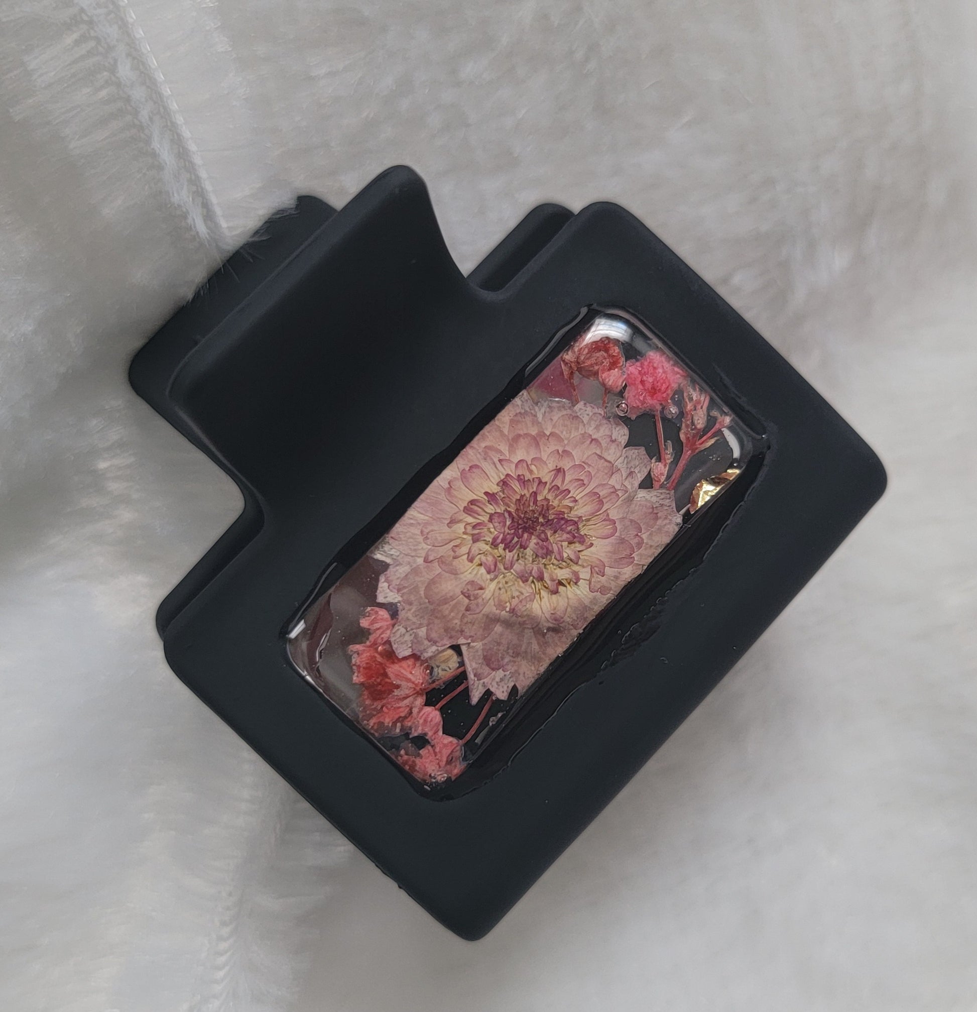 A black 2-inch claw clip with lavender and pink pressed flowers cast in resin within an open space in the hair clip.