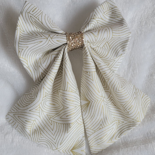 A handmade pet bow with a soft cotton print of abstract gold geometric lines on off-white background, gold blue glitter center sailor bow style with long showy tails.