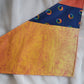 A multicolored pet bandana with stripes of cotton fabric, featuring a soft orange ombre with subtle sky design and contrasting deep blue stripe with rainbow spectrum moons. Laying flat showing side that has more light yellow-orange.