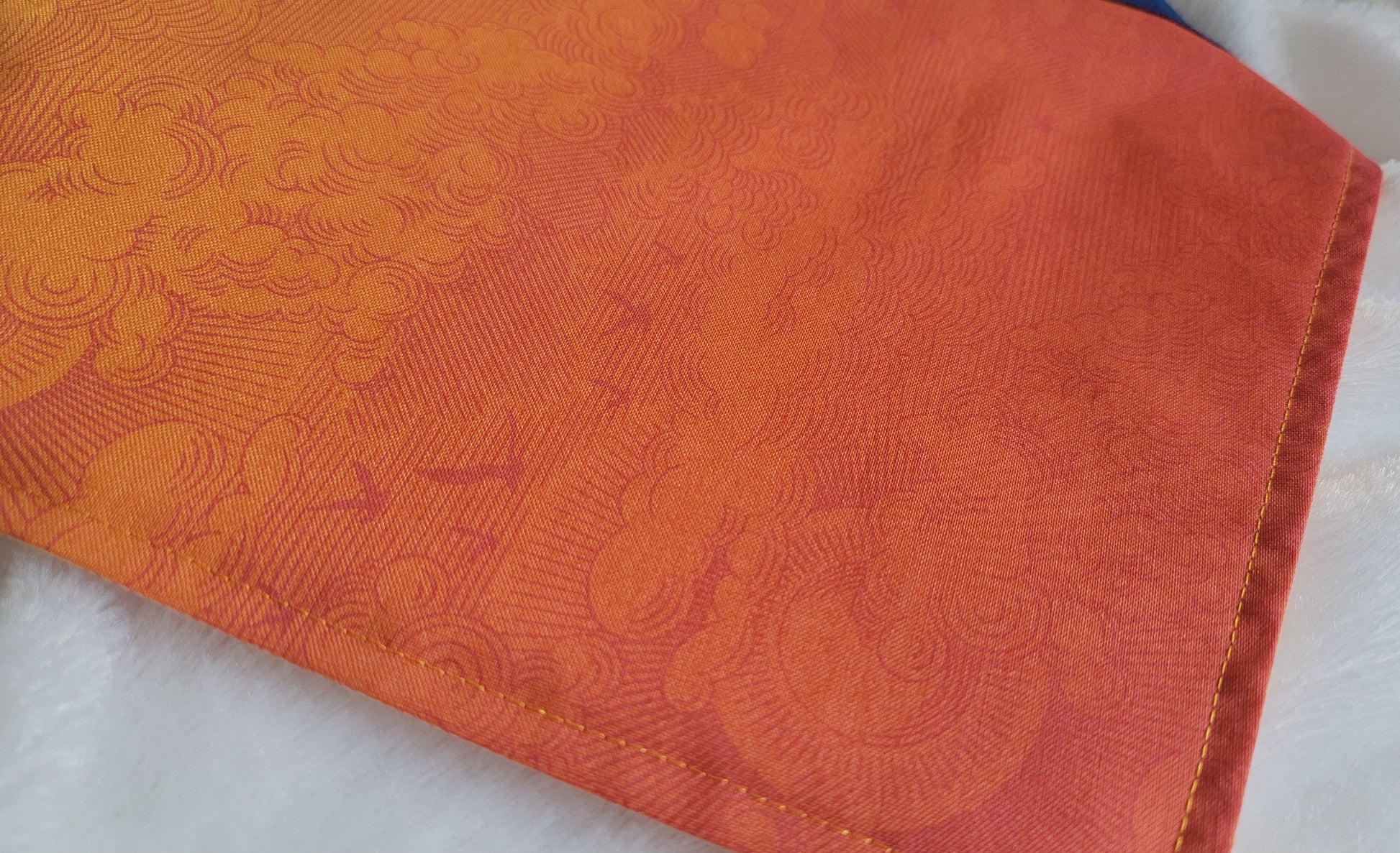 Close up of the orange ombre fabric, on a part with more deep orange, showing the sky print which has suns and clouds and seabirds and stars in contrasting shades of orange.