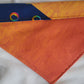 A multicolored pet bandana with stripes of cotton fabric, featuring a soft orange ombre with subtle sky design and contrasting deep blue stripe with rainbow spectrum moons. Showing side that has more deep orange, top edge is folded over to show the reverse side.