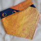 A multicolored pet bandana with stripes of cotton fabric, featuring a soft orange ombre with subtle sky design and contrasting deep blue stripe with rainbow spectrum moons. Showing side that has more light yellow-orange, with corners folded under and top edge folded over to show the reverse side.
