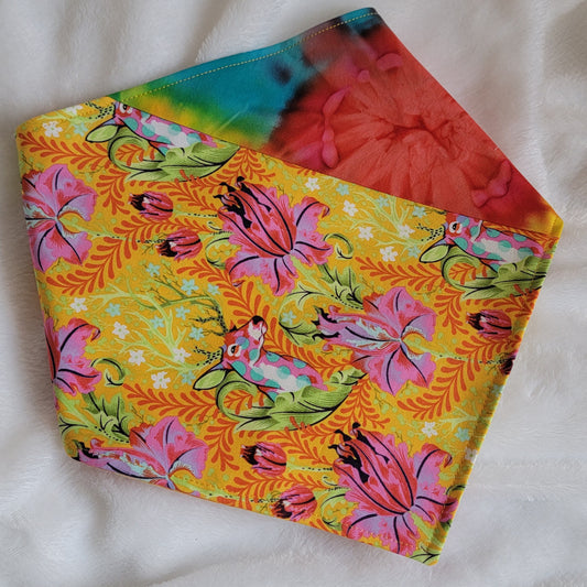 A multicolored pet bandana with stripes of cotton fabric featuring colorful rainbow tie-dye and vibrant floral stag print. Corners folded under showing side that has wider stripe of stag floral fabric.