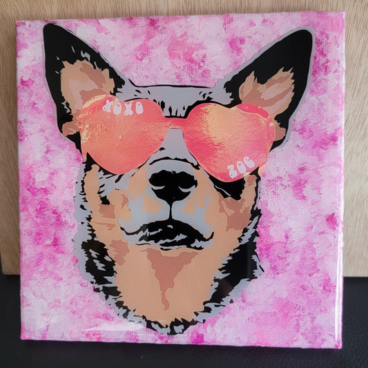 Portrait of a tan and merle cattle dog wearing pink heart shaped sunglasses made with layers of vinyl on a small canvas with mottled pink acrylic paint, sealed in epoxy resin.