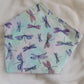 A reversible pet bandana with one side featuring multicolor dragonflies on soft aqua pastel background and the other side vibrant pink and purple waterlilies with dragonflies. Bandana is displayed on white background with corners folded under, showing the side with multicolor dragonflies.