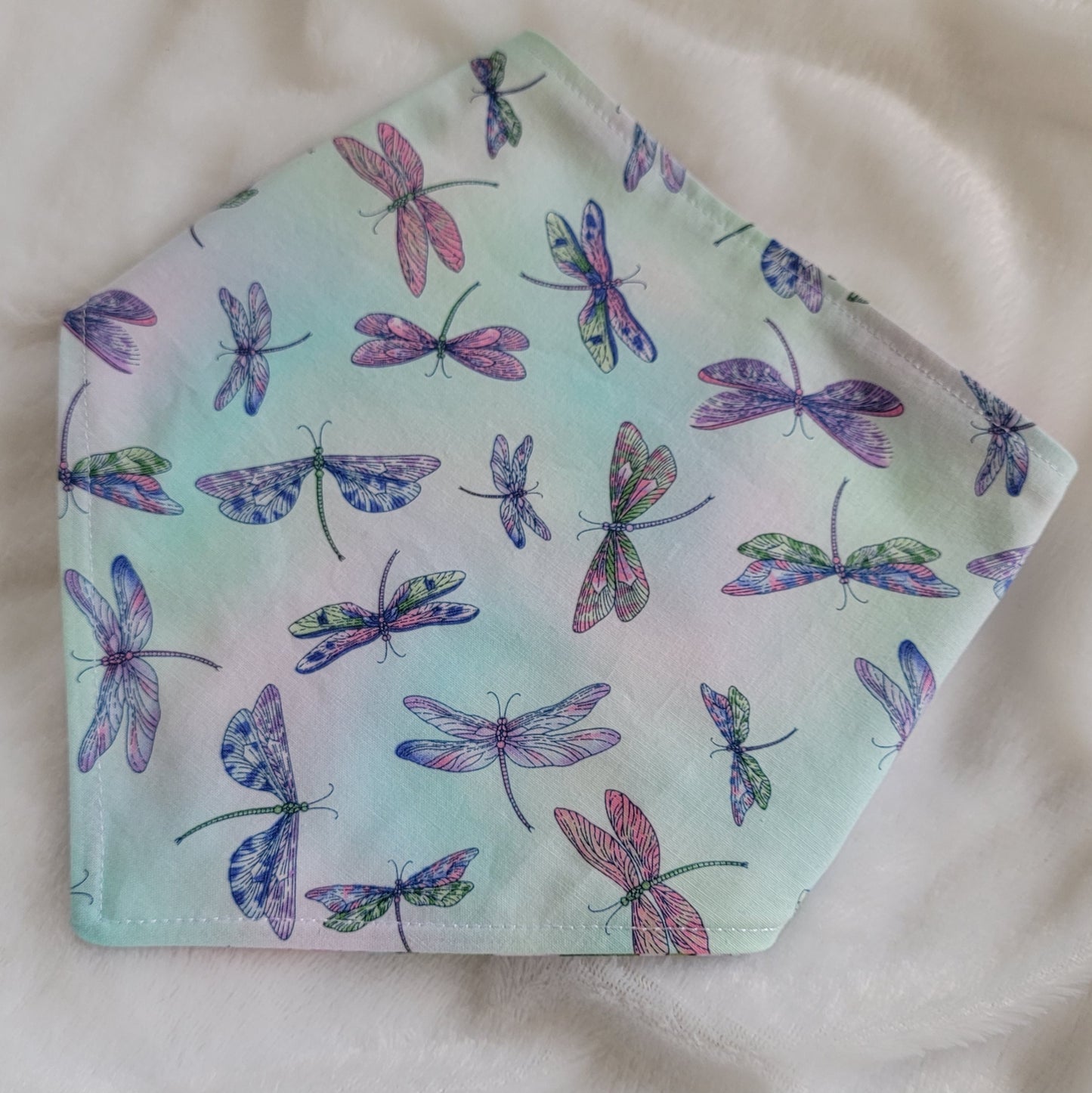 A reversible pet bandana with one side featuring multicolor dragonflies on soft aqua pastel background and the other side vibrant pink and purple waterlilies with dragonflies. Bandana is displayed on white background with corners folded under, showing the side with multicolor dragonflies.