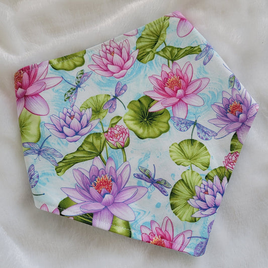 A reversible pet bandana with one side featuring multicolor dragonflies on soft aqua pastel background and the other side vibrant pink and purple waterlilies with dragonflies. Bandana is displayed on white background with corners folded under, showing the side with pink and purple waterlilies.