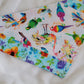 Handmade bandana featuring colorful tropical birds and floral prints patched together in stripes, unique on each side. Displayed laying flat on a white background.