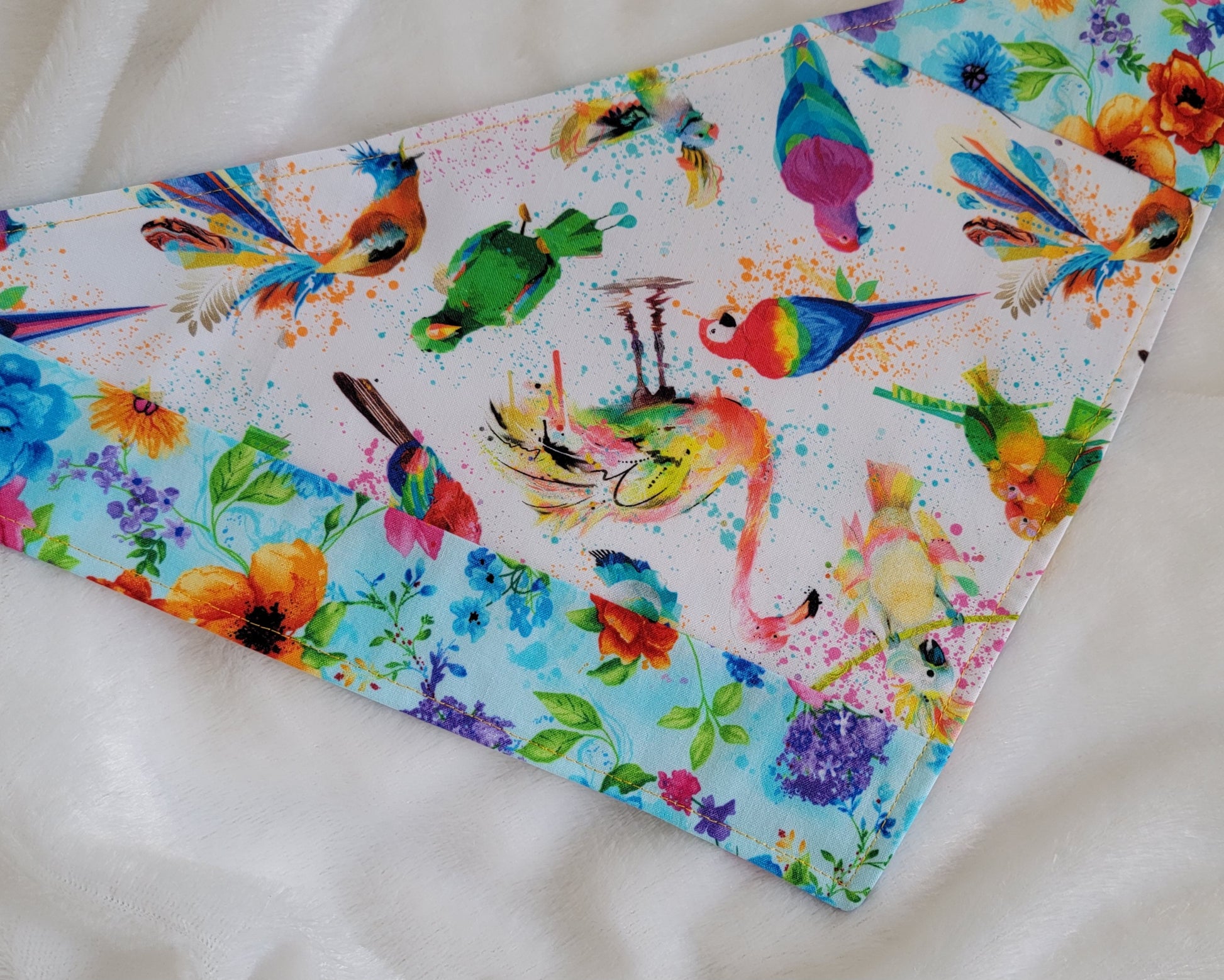 Handmade bandana featuring colorful tropical birds and floral prints patched together in stripes, unique on each side. Displayed laying flat on a white background.
