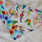 Handmade bandana featuring colorful tropical birds and floral prints patched together in stripes, unique on each side. Displayed laying flat on a white background.
