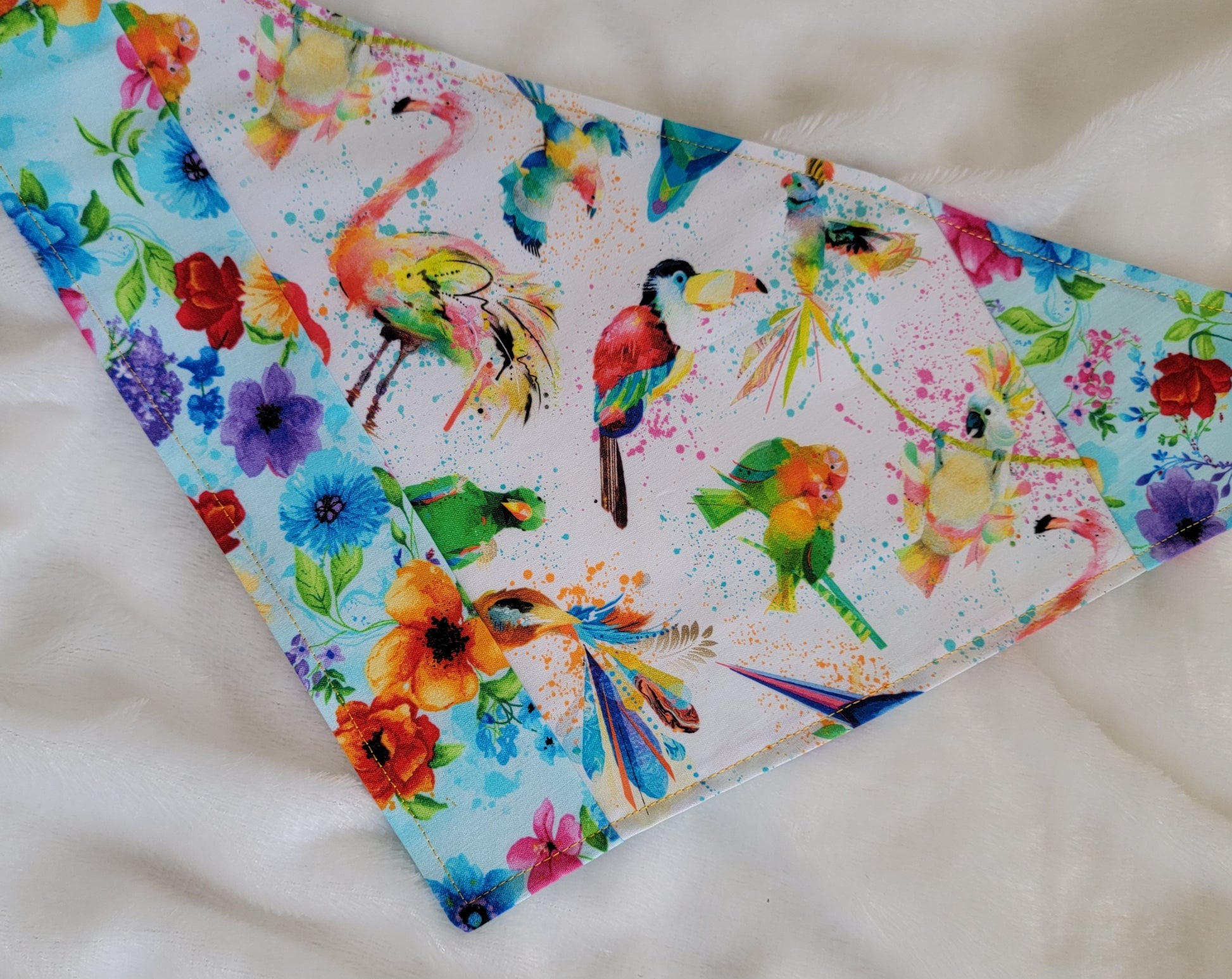 Handmade bandana featuring colorful tropical birds and floral prints patched together in stripes, unique on each side. Displayed laying flat on a white background.
